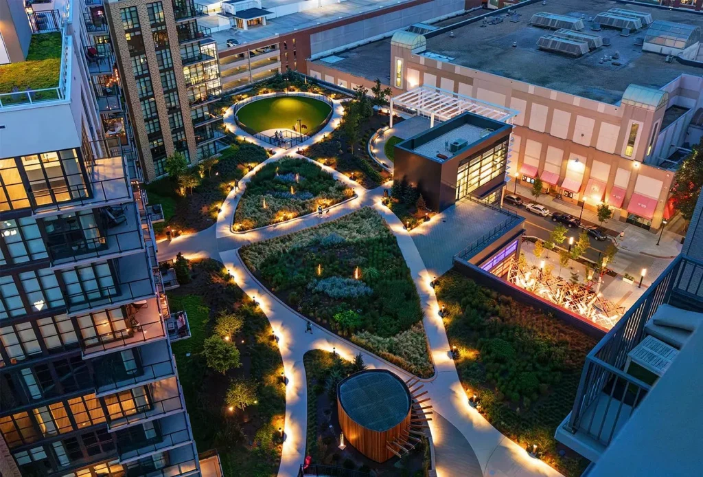 11 نکته کلیدی برای طراحی فضاهای عمومی موفق 10 روف گاردن شهری مدرن با نورپردازی زیبا در شب، میان ساختمانها.