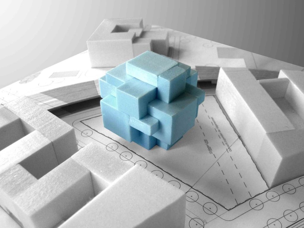 10 راهکار طلایی برای ساخت مدلهای مفهومی معماری 2 مدل معماری شامل یک مکعب پازلمانند آبی و ساختمانهای فومی سفید روی نقشه.